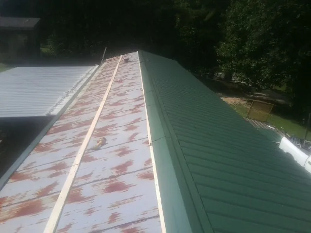 Old rusted panels beside newly installed green metal roofing — Wind Damage Roof Repair by Roofing Brothers in Laurel